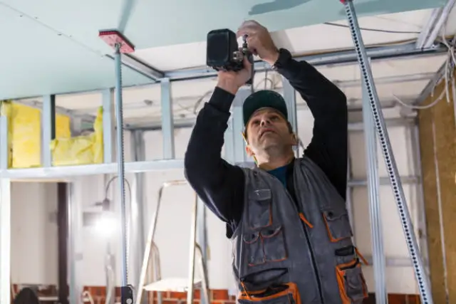 Obrero instalando un cielorraso con placas de Durlock en un ambiente interior, utilizando herramientas especializadas para construcción en seco.