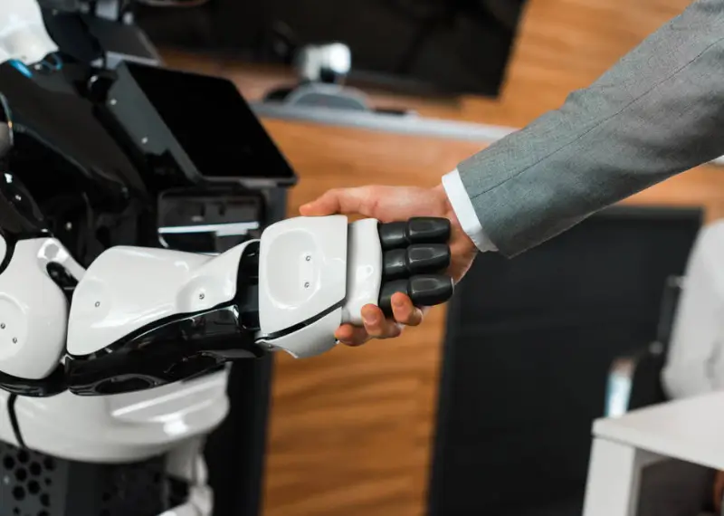 Ejecutivo estrechando la mano de un robot como símbolo de la implementación de IA en empresas